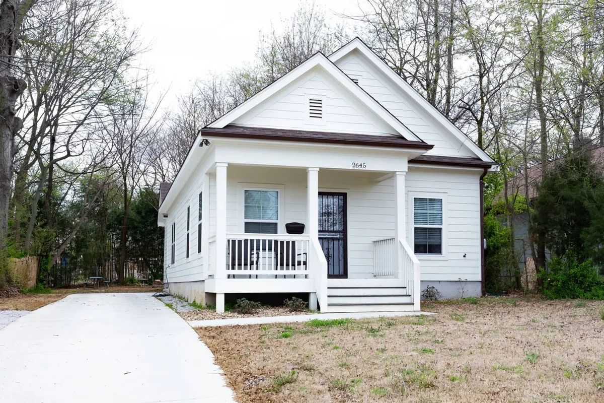 This image captures the exterior front porch with white siding, a welcoming doorway, and a neatly landscaped yard. The setup suggests easy access from the parking area and a homey arrival sequence.