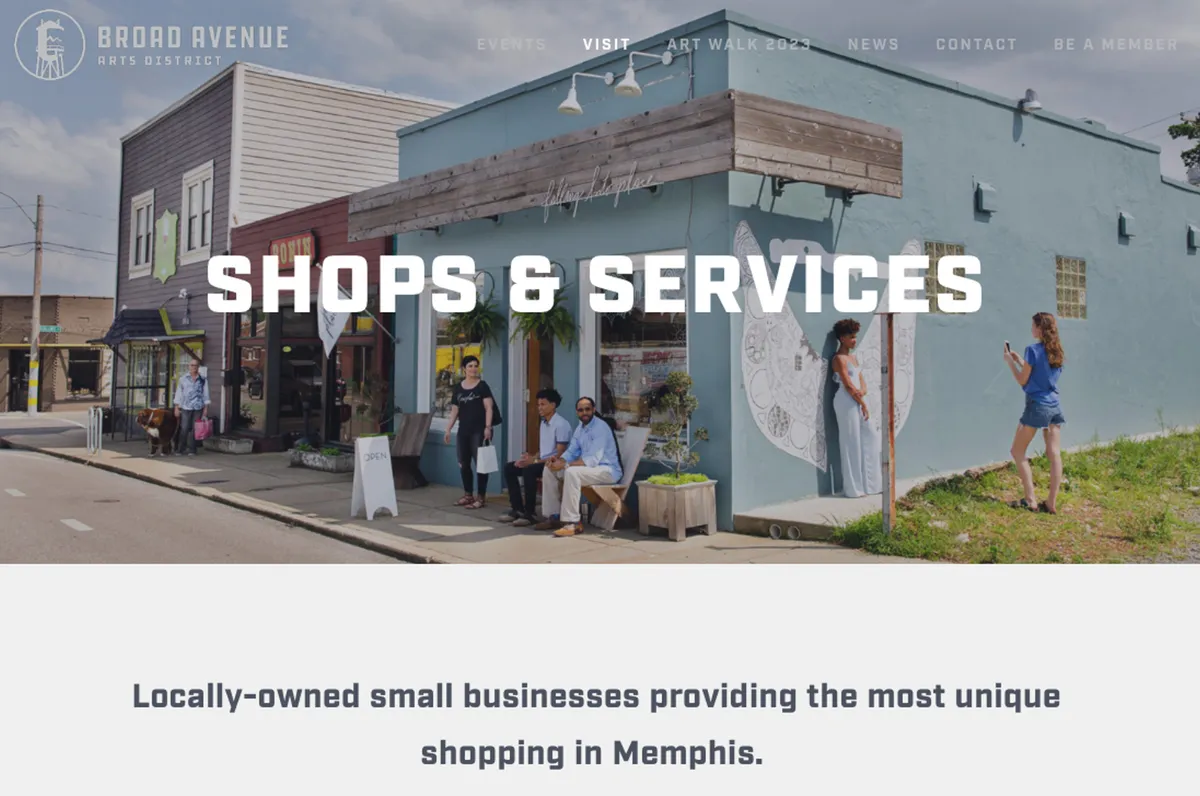 A lively street scene featuring colorful storefronts, people chatting and shopping outside, and a large artistic mural adorning a building wall. The atmosphere is bustling, with locals and visitors enjoying the community vibe and creative displays.
